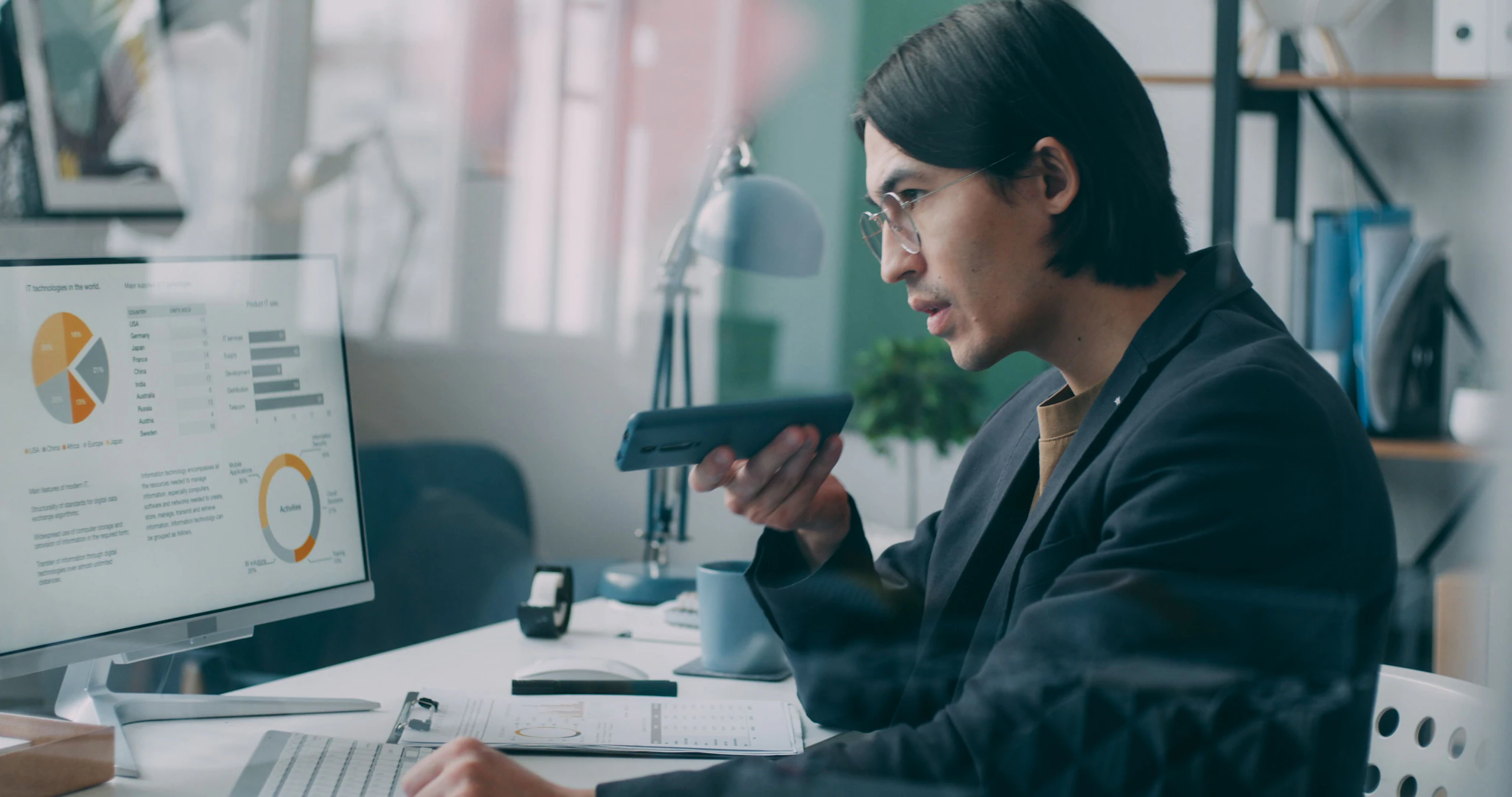 An analyst at a monitor filled with dashboard charts, holding a tablet in one hand.