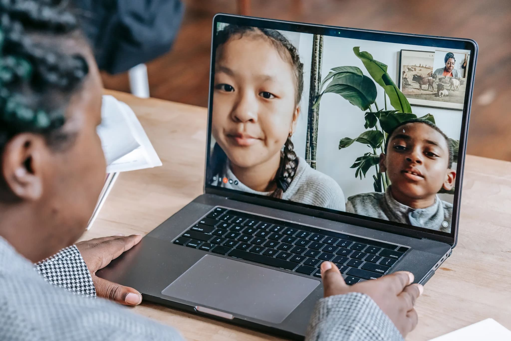 Over-the-shoulder view of someone at a laptop on a video call with two children on screen.