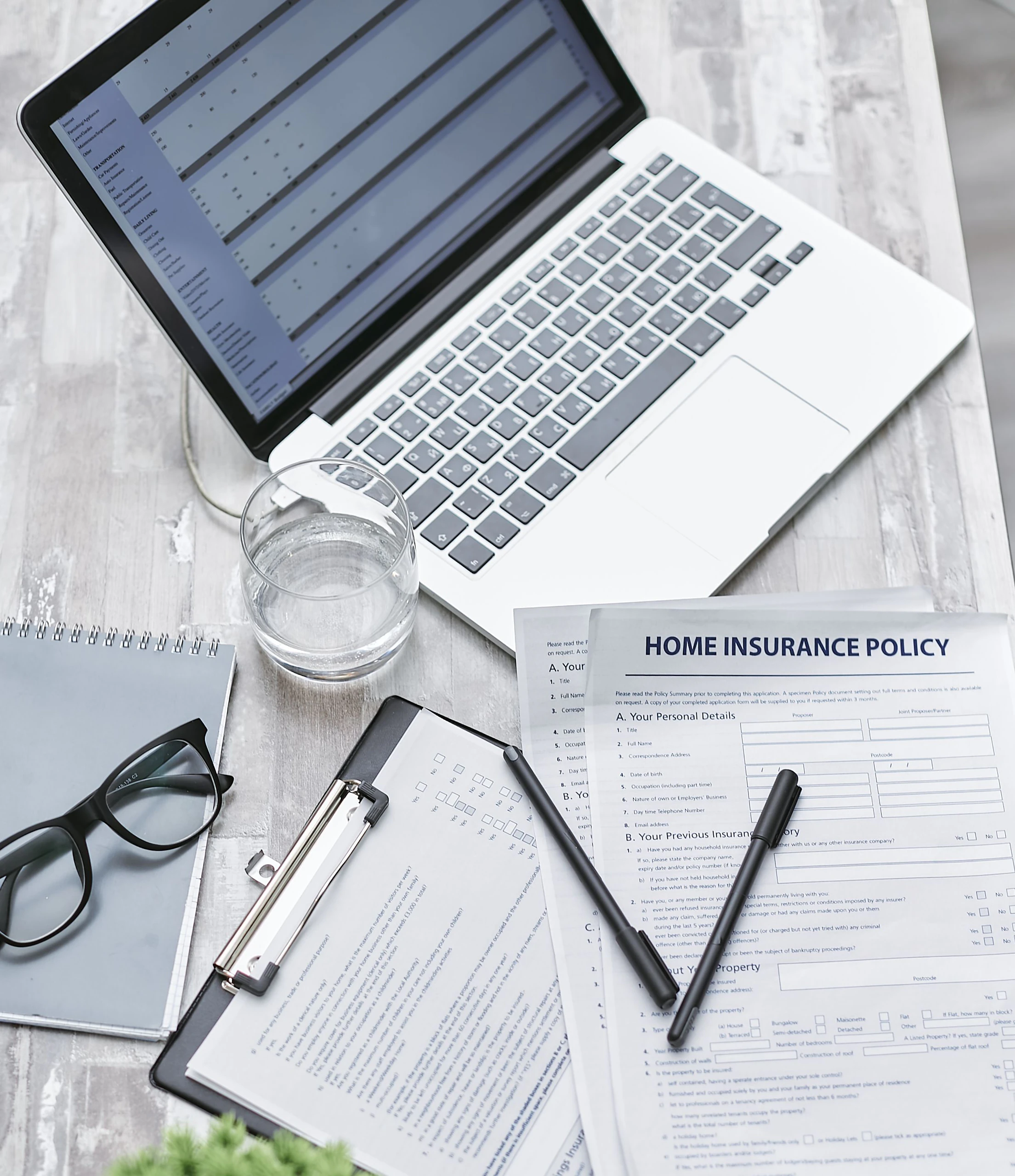 An insurance policy and paperwork on a desk beside a laptop.