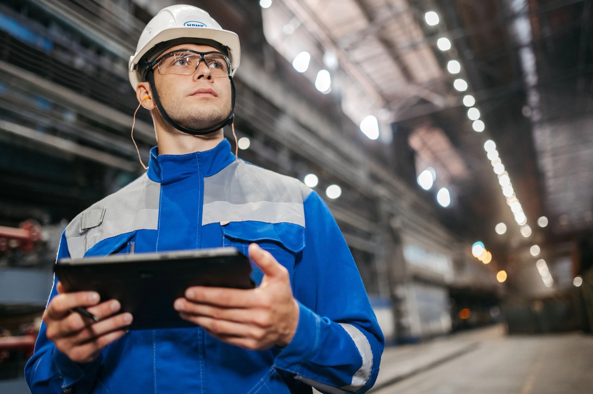 An engineer in a hard hat using a tablet on a factory floor.